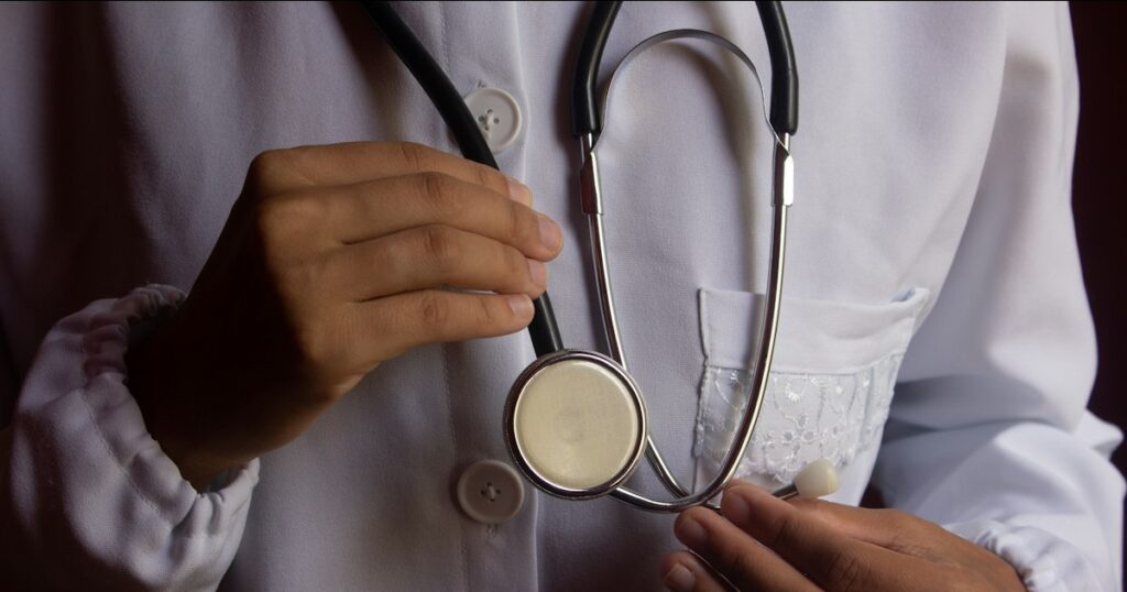 Médica de jaleco branco segurando um estetoscópio