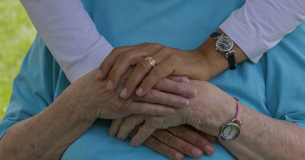 Mãos de uma pessoa mais jovem sobre as mãos de uma idosa, em gesto de cuidado